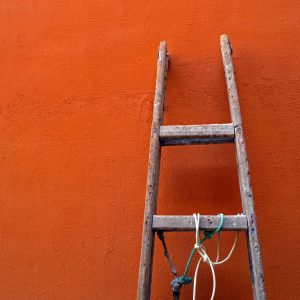 A wooden loft ladder leaning against an orange wall.